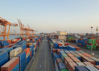 Porto commerciale con container all'alba: le merci importate nell'UE ora pagano la CO2 con il CBAM
