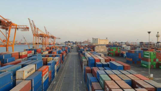 Porto commerciale con container all'alba: le merci importate nell'UE ora pagano la CO2 con il CBAM