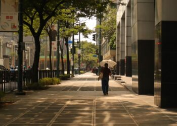Persona con ombrello in una strada di città assolata