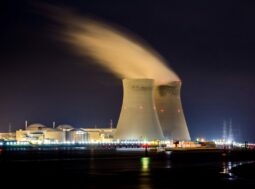 Energia nucleare: centrale illuminata di notte con la torre di raffreddamento che rilascia vapore accanto a un fiume