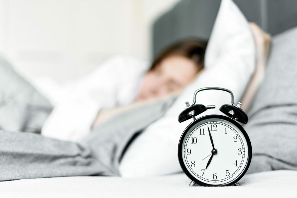 Ora legale permanente: una sveglia sul comodino accanto a una persona che dorme al mattino