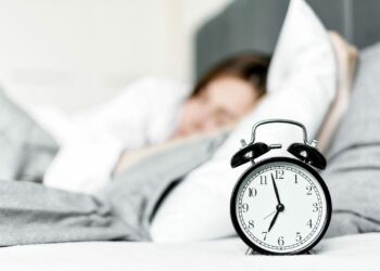 Ora legale permanente: una sveglia sul comodino accanto a una persona che dorme al mattino